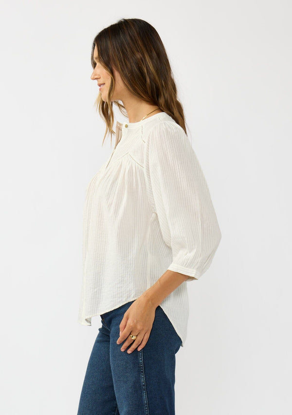 [Color: Cream/Black] A side facing image of a brunette model wearing a boho striped button front blouse with a pintuck yoke, lattice trim, and voluminous sleeves. 