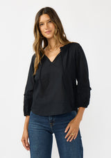 [Color: Black] A front facing image of a brunette model wearing a black cotton blouse with tonal embroidered 3/4 sleeves and a split v-neckline with tie detail. 