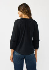 [Color: Black] A back facing image of a brunette model wearing a black cotton blouse with tonal embroidered 3/4 sleeves and a split v-neckline with tie detail. 