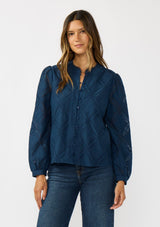[Color: Navy] A front facing image of a brunette model wearing a navy blue button up blouse with a diamond lattice pattern and long sleeves with button cuffs. A versatile top for the office and weekend casual outings. 