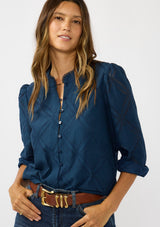 [Color: Navy] A front facing image of a brunette model wearing a navy blue button up blouse with a diamond lattice pattern and long sleeves with button cuffs. A versatile top for the office and weekend casual outings. 