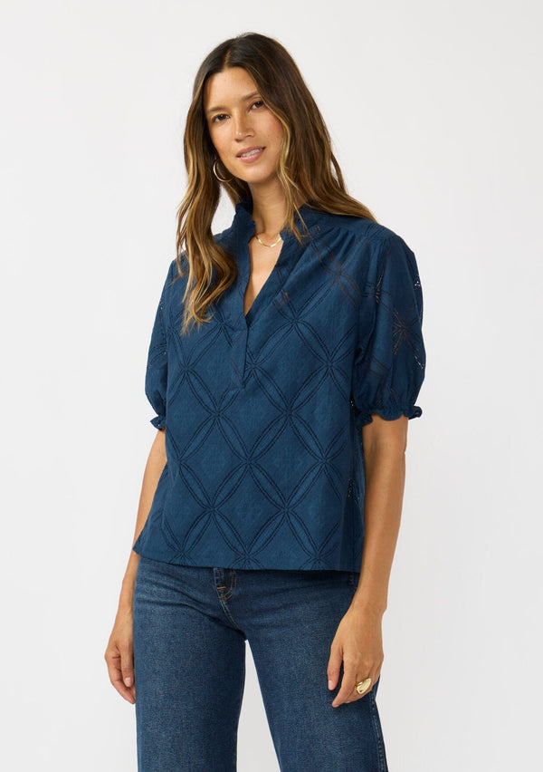 [Color: Navy] A front facing image of a brunette model wearing a navy puff sleeve top with a diamond lattice pattern, ruffled details, and a split v-neckline. 