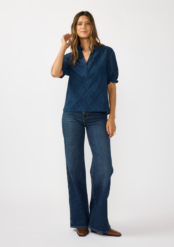 [Color: Navy] A front facing image of a brunette model wearing a navy puff sleeve top with a diamond lattice pattern, ruffled details, and a split v-neckline. 