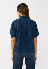[Color: Navy] A back facing image of a brunette model wearing a navy puff sleeve top with a diamond lattice pattern, ruffled details, and a split v-neckline. 