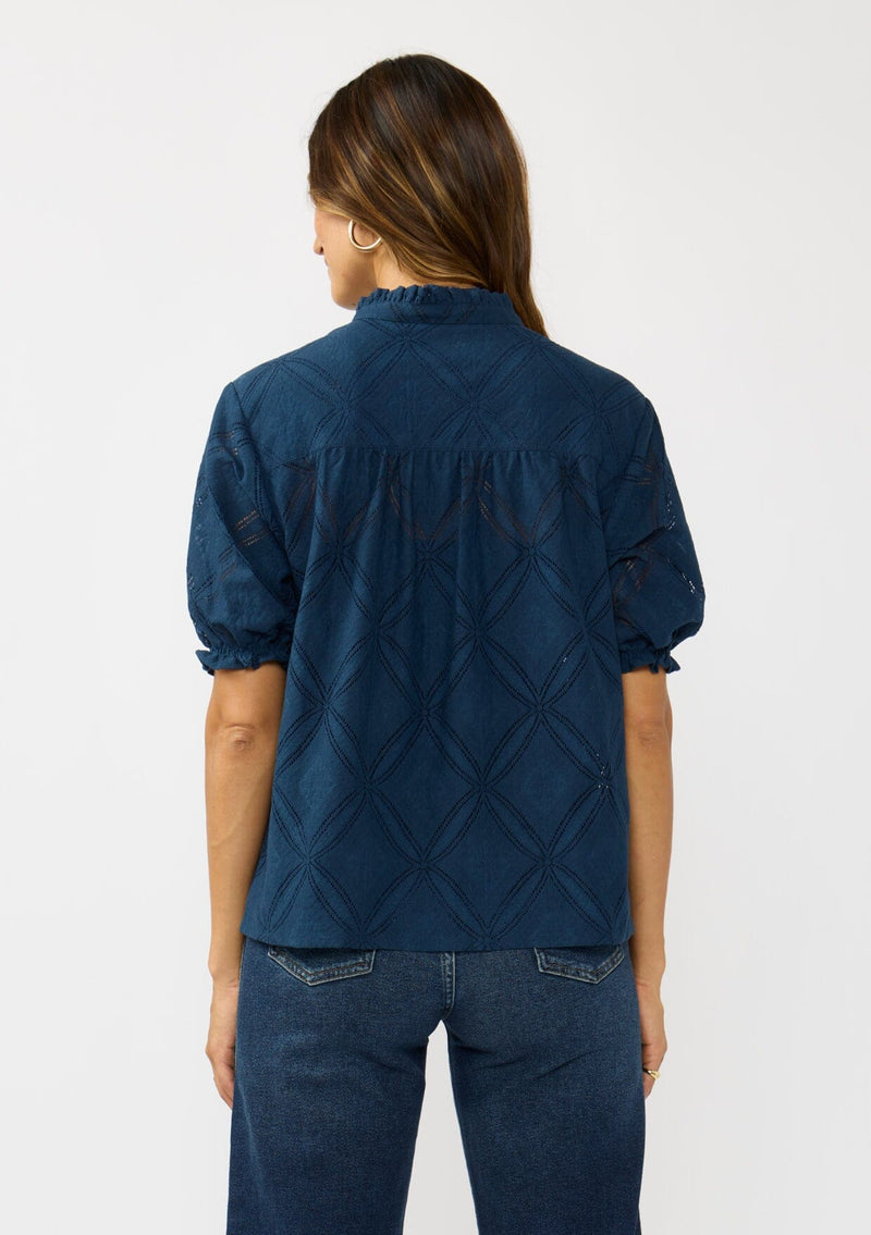[Color: Navy] A back facing image of a brunette model wearing a navy puff sleeve top with a diamond lattice pattern, ruffled details, and a split v-neckline. 
