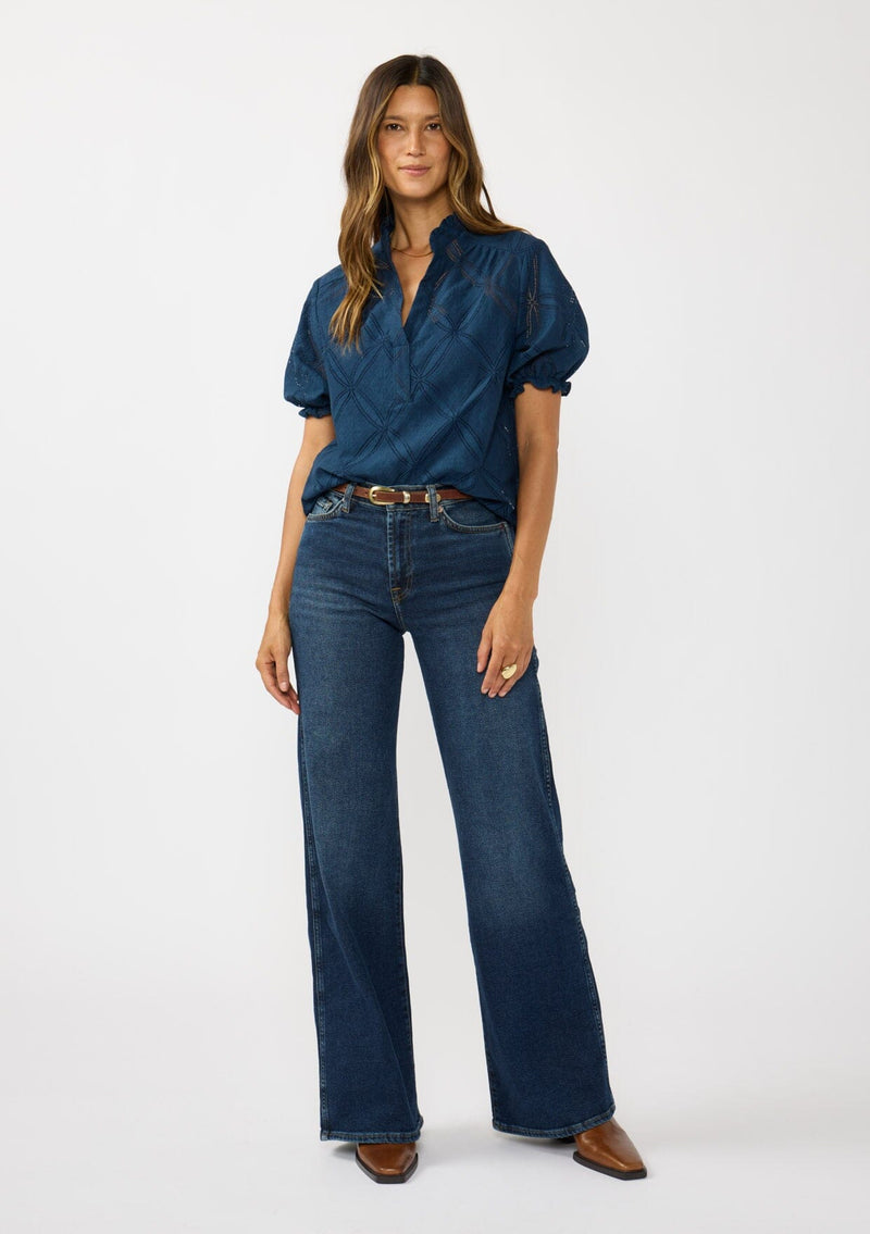 [Color: Navy] A front facing image of a brunette model wearing a navy puff sleeve top with a diamond lattice pattern, ruffled details, and a split v-neckline. 