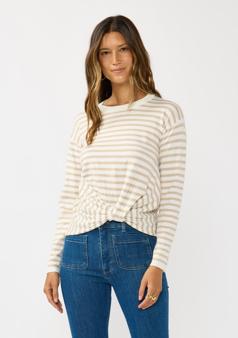 [Color: Ivory/Tan] A front facing image of a brunette model wearing a classic ivory and tan brown striped knit pullover sweater. With long sleeves, a drop shoulder, a crew neckline, and a twist front detail at the waist. 