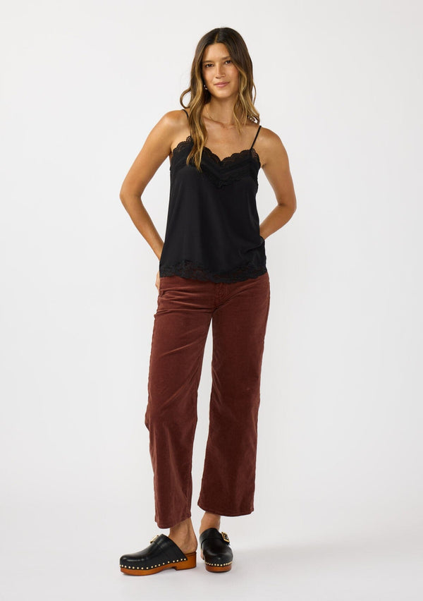 [Color: Black] A front facing image of a brunette model wearing a black cami with lace trims on the neck and hem, adjustable spaghetti straps, and a v-neckline. 