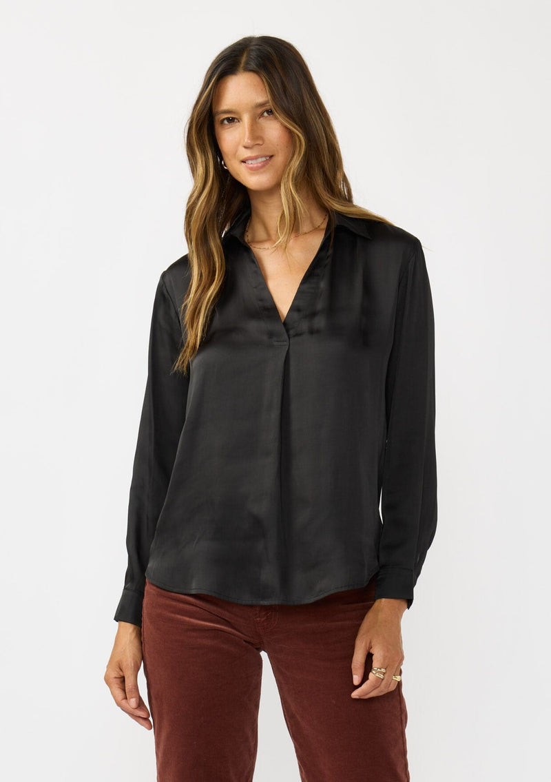 [Color: Black] A front facing image of a brunette model wearing a silky poly satin blouse with a split v-neckline, collar, and long sleeves with button cuffs. 
