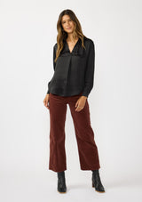 [Color: Black] A front facing image of a brunette model wearing a silky poly satin blouse with a split v-neckline, collar, and long sleeves with button cuffs. 