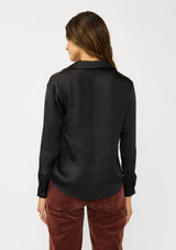 [Color: Black] A back facing image of a brunette model wearing a silky poly satin blouse with a split v-neckline, collar, and long sleeves with button cuffs. 