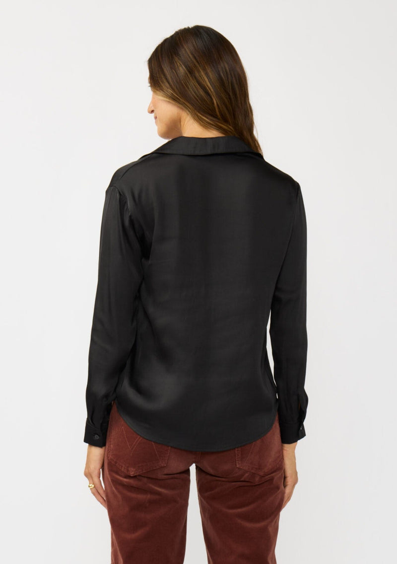 [Color: Black] A back facing image of a brunette model wearing a silky poly satin blouse with a split v-neckline, collar, and long sleeves with button cuffs. 
