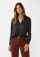 [Color: Black] A front facing image of a brunette model wearing a silky poly satin blouse with a split v-neckline, collar, and long sleeves with button cuffs. 