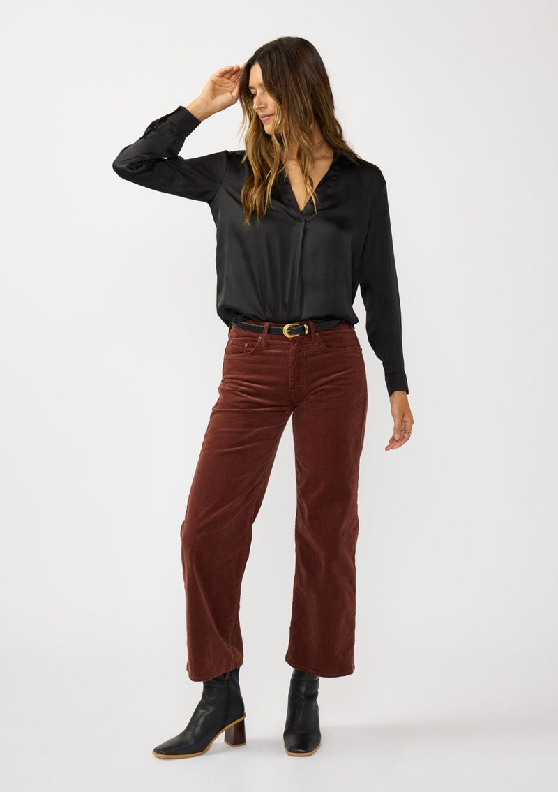 [Color: Black] A front facing image of a brunette model wearing a silky poly satin blouse with a split v-neckline, collar, and long sleeves with button cuffs. 