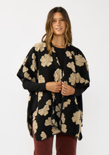 [Color: Black/Taupe] A front facing image of a brunette model wearing a fuzzy floral poncho with sleeve openings and an open front. A unique and casual throw on for the fall season. 