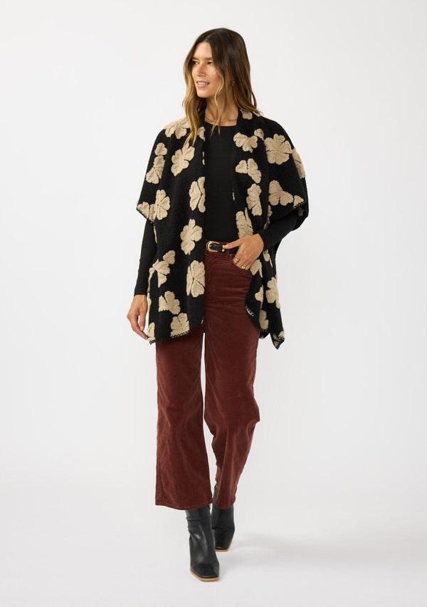 [Color: Black/Taupe] A front facing image of a brunette model wearing a fuzzy floral poncho with sleeve openings and an open front. A unique and casual throw on for the fall season. 