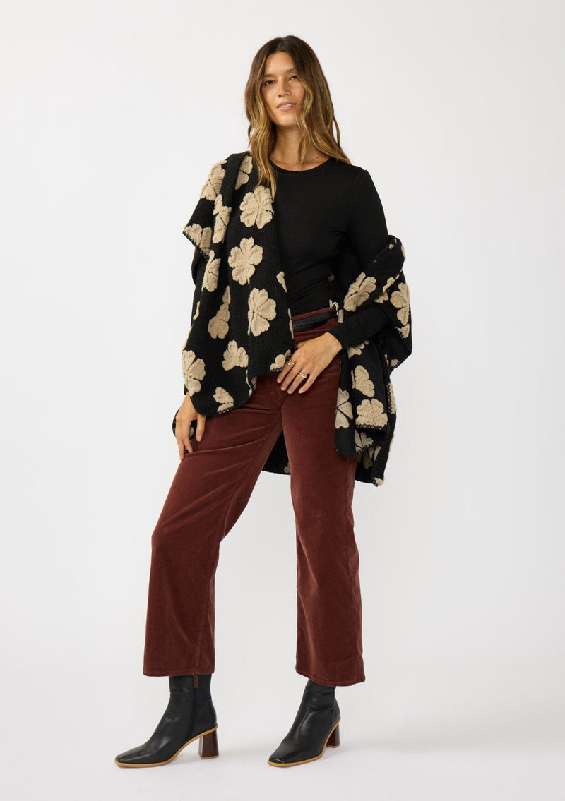 [Color: Black/Taupe] A front facing image of a brunette model wearing a fuzzy floral poncho with sleeve openings and an open front. A unique and casual throw on for the fall season. 