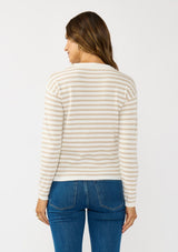 [Color: Ivory/Tan] A back facing image of a brunette model wearing a classic ivory and tan brown striped knit pullover sweater. With long sleeves, a drop shoulder, a crew neckline, and a twist front detail at the waist. 