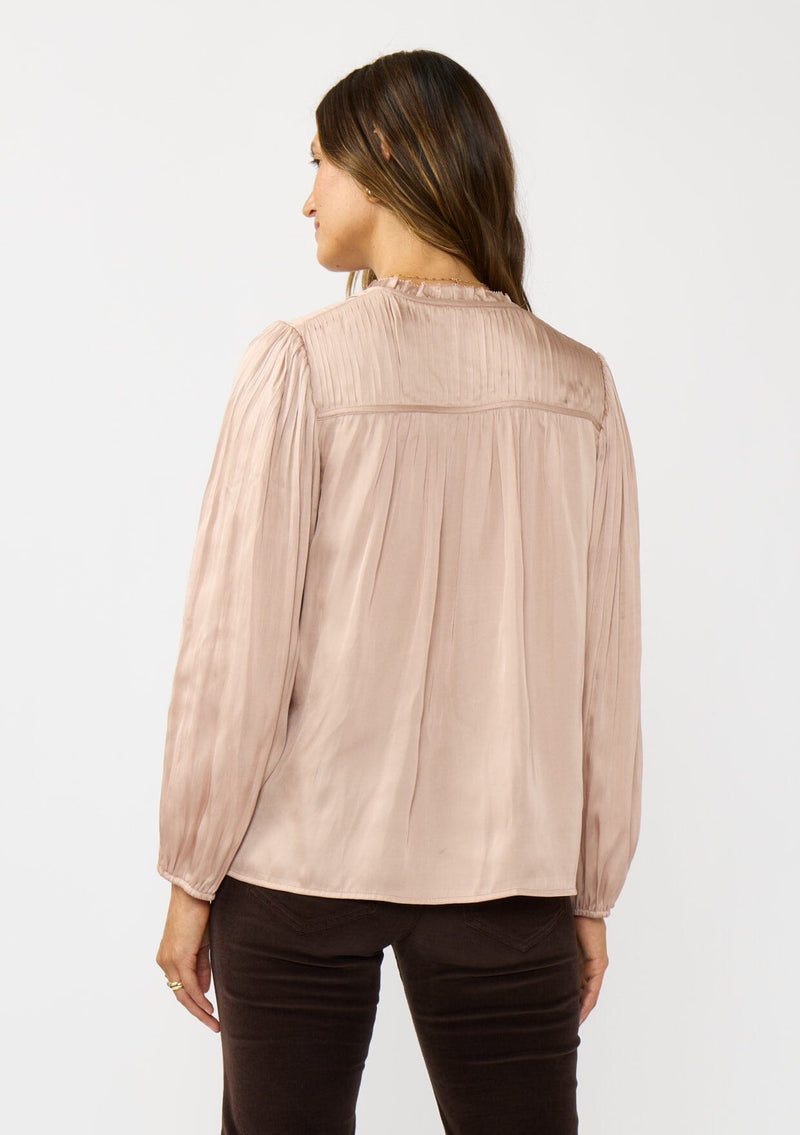 [Color: Champagne] A back facing image of a brunette model wearing silky rose gold blouse with a pleated yoke and sleeve. Featuring a relaxed split v-neckline for a laid back vibe. Effortless and charming for the Holiday season. 