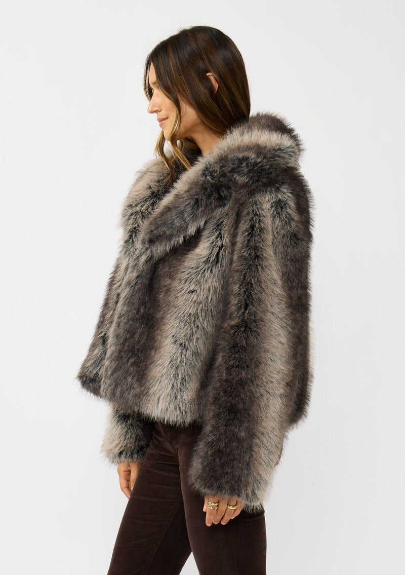[Color: Charcoal] A side facing image of a brunette model wearing an ombre charcoal faux fur coat with a chic collar and cozy fit. Perfect for fall to winter styling. 