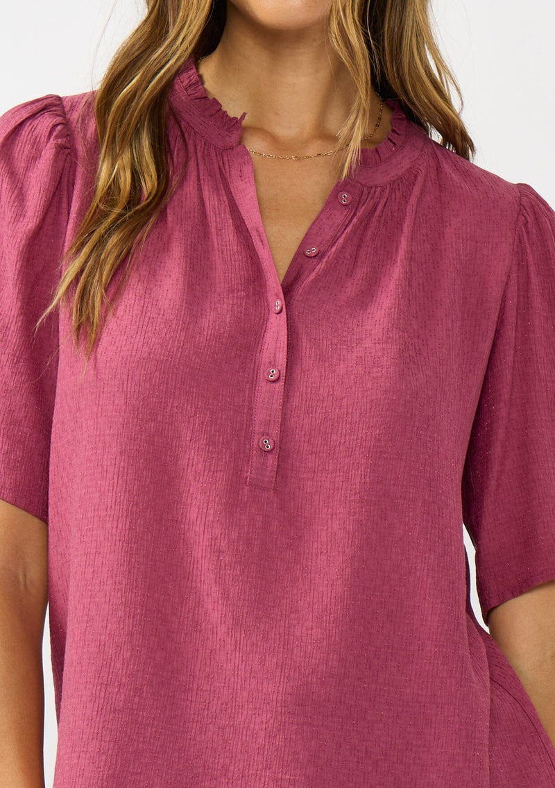 [Color: Berry] A detail image of a brunette model wearing a pink puff sleeve top with gold metallic threads, a smocked detail on sleeve, and a button front. 