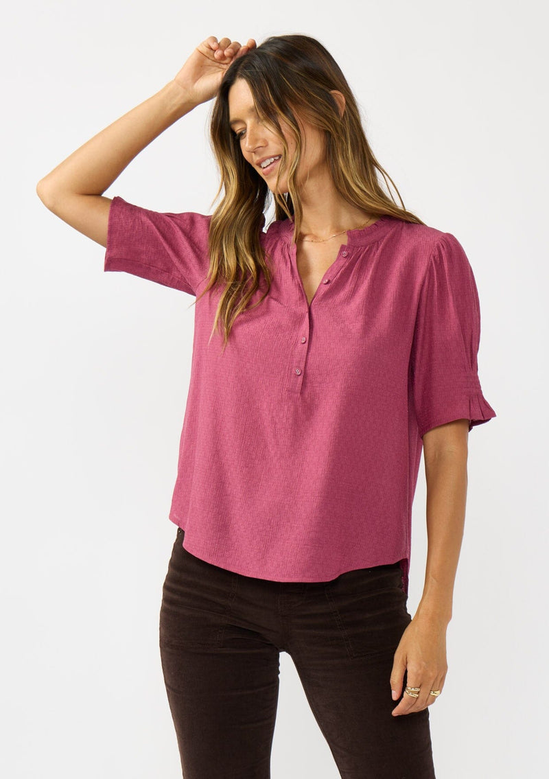[Color: Berry] A front facing image of a brunette model wearing a pink puff sleeve top with gold metallic threads, a smocked detail on sleeve, and a button front. 