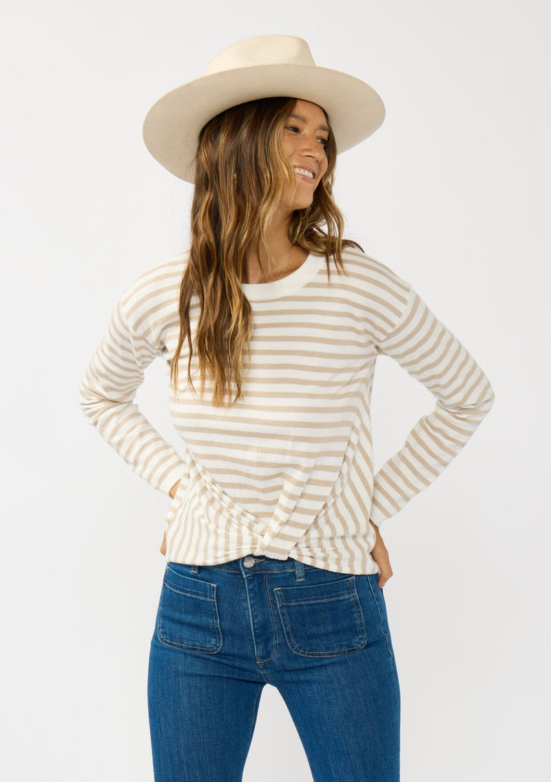 [Color: Ivory/Tan] A front facing image of a brunette model wearing a classic ivory and tan brown striped knit pullover sweater. With long sleeves, a drop shoulder, a crew neckline, and a twist front detail at the waist. 
