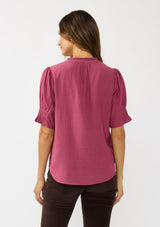 [Color: Berry] A back facing image of a brunette model wearing a pink puff sleeve top with gold metallic threads, a smocked detail on sleeve, and a button front. 