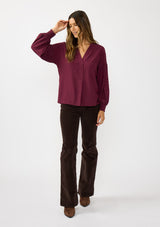 [Color: Merlot] A front facing image of a brunette model wearing burgundy blouse with embroidery. Featuring long bishop sleeves, smocked cuffs, and a split v-neckline. An elevated boho blouse for the office or casual outings. 