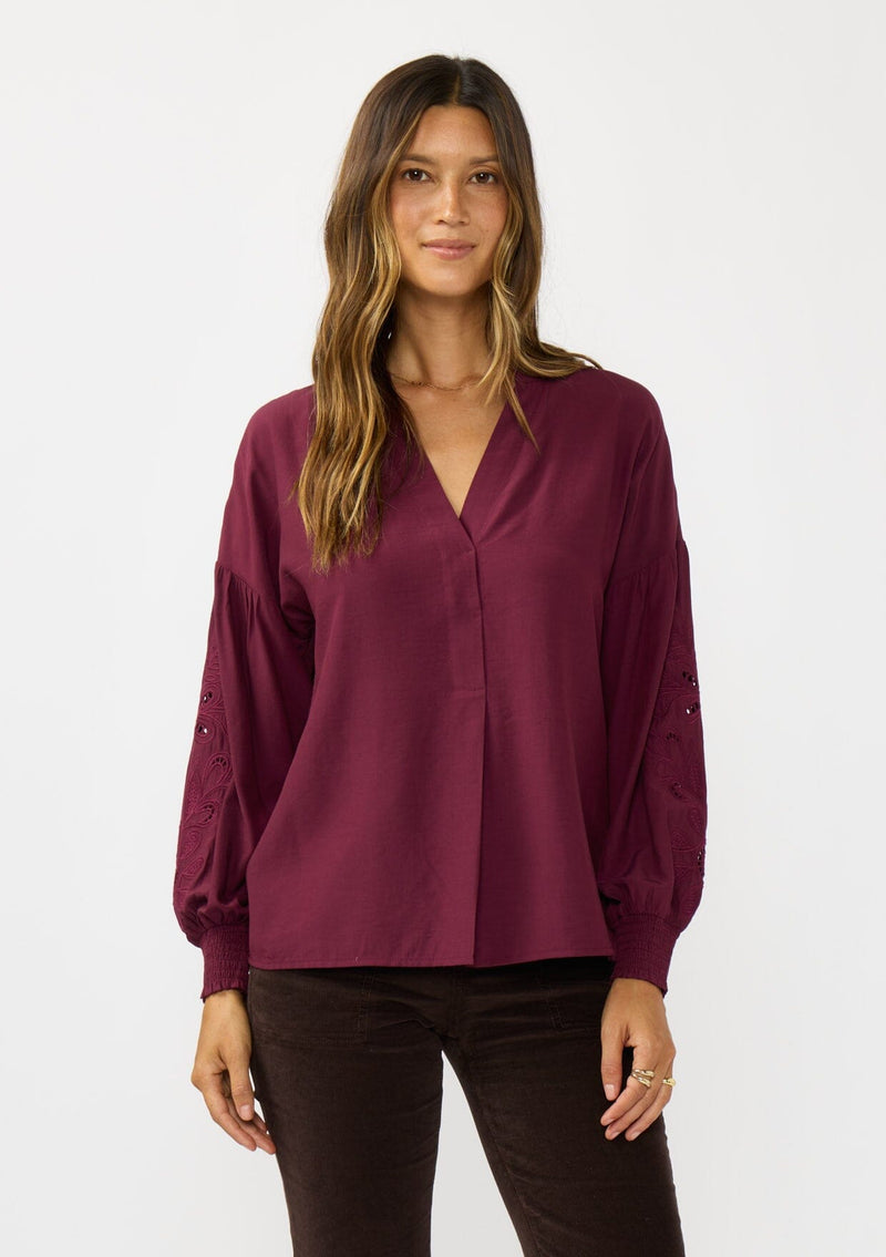 [Color: Merlot] A front facing image of a brunette model wearing burgundy blouse with embroidery. Featuring long bishop sleeves, smocked cuffs, and a split v-neckline. An elevated boho blouse for the office or casual outings. 