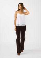 [Color: Chalk] A front facing image of a brunette model wearing a white cami with lace trims on the neck and hem, adjustable spaghetti straps, and a v-neckline. 