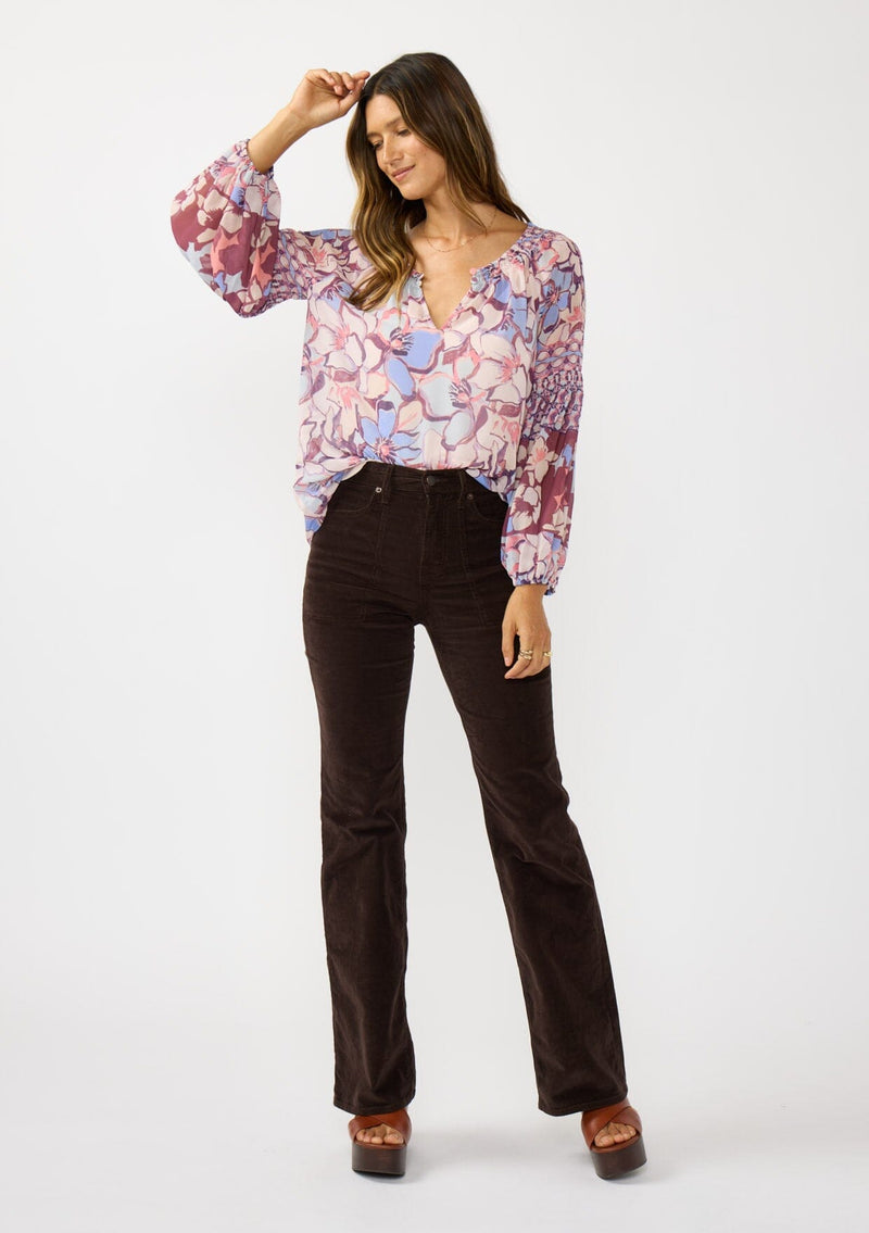 [Color: Natural/Dusty Blue] A front facing image of a brunette model wearing a pink and blue floral chiffon blouse with smocking on the neck and sleeve, and a split v-neckline with button closure. A standout flowy top for the fall season. 