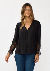 [Color: Black] A front facing image of a brunette model wearing a solid black blouse with lace accented sleeves, button front, and v-neckline. A classic and versatile boho blouse with an elevated touch. 