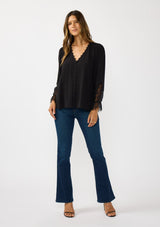 [Color: Black] A front facing image of a brunette model wearing a solid black blouse with lace accented sleeves, button front, and v-neckline. A classic and versatile boho blouse with an elevated touch. 