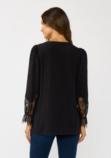 [Color: Black] A back facing image of a brunette model wearing a solid black blouse with lace accented sleeves, button front, and v-neckline. A classic and versatile boho blouse with an elevated touch. 