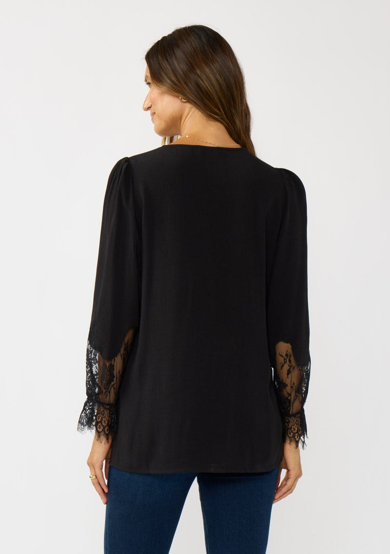 [Color: Black] A back facing image of a brunette model wearing a solid black blouse with lace accented sleeves, button front, and v-neckline. A classic and versatile boho blouse with an elevated touch. 
