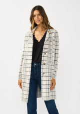 [Color: Cream/Black] A front facing image of a brunette model wearing a fuzzy statement sweater coat in a cream and black plaid print. With long sleeves, a notched collar, a snap button front, and side patch pockets. 