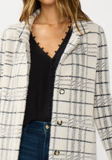 [Color: Cream/Black] A detail image of a brunette model wearing a fuzzy statement sweater coat in a cream and black plaid print. With long sleeves, a notched collar, a snap button front, and side patch pockets. 