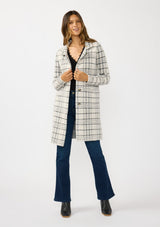 [Color: Cream/Black] A front facing image of a brunette model wearing a fuzzy statement sweater coat in a cream and black plaid print. With long sleeves, a notched collar, a snap button front, and side patch pockets. 