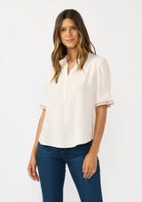 [Color: Pale Rose] A front facing image of a brunette model wearing a light pink pink top with embroidered details on the puff sleeves, a button front, and a ruffled neck accent. 