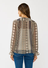[Color: Natural/Navy] A back facing image of a brunette model wearing a beige striped floral pattern blouse with a relaxed boho silhouette, split v-neckline with ties, and long sleeves with ruffled elastic cuffs. 