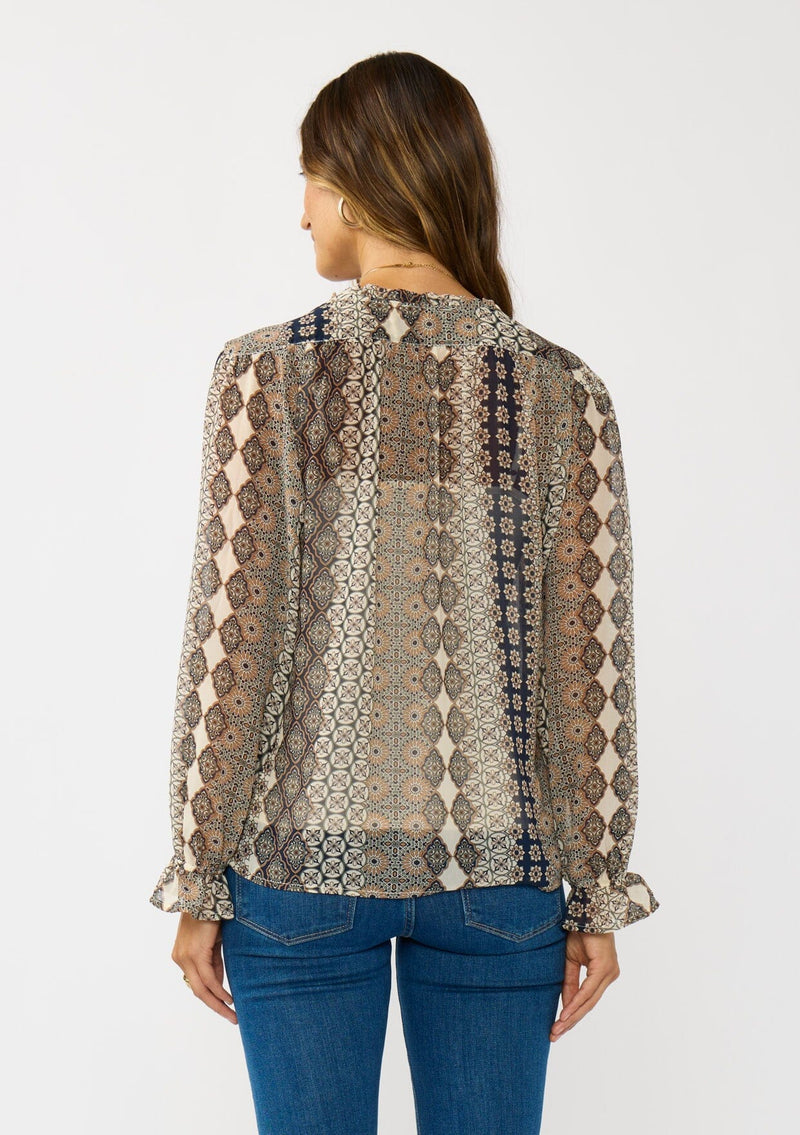 [Color: Natural/Navy] A back facing image of a brunette model wearing a beige striped floral pattern blouse with a relaxed boho silhouette, split v-neckline with ties, and long sleeves with ruffled elastic cuffs. 