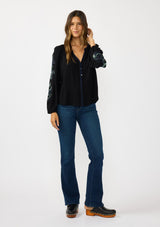 [Color: Black] A front facing image of a brunette model wearing a flowy black blouse with colorful embroidered sleeve details, a button front, and blanket stitch detailing. Perfect for fall styling. 