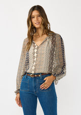 [Color: Natural/Navy] A front facing image of a brunette model wearing a beige striped floral pattern blouse with a relaxed boho silhouette, split v-neckline with ties, and long sleeves with ruffled elastic cuffs. 