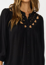 [Color: Black] A detail image of a brunette model wearing black cutout blouse with 3/4 sleeves and a button front. 