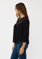 [Color: Black] A side facing image of a brunette model wearing black cutout blouse with 3/4 sleeves and a button front. 