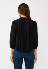 [Color: Black] A back facing image of a brunette model wearing black cutout blouse with 3/4 sleeves and a button front. 
