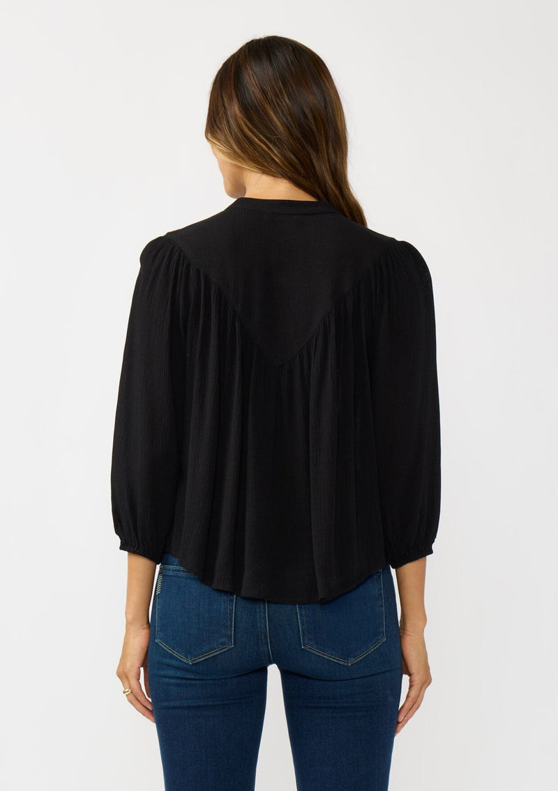 [Color: Black] A back facing image of a brunette model wearing black cutout blouse with 3/4 sleeves and a button front. 