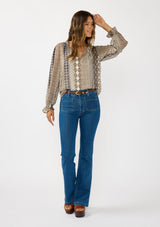 [Color: Natural/Navy] A front facing image of a brunette model wearing a beige striped floral pattern blouse with a relaxed boho silhouette, split v-neckline with ties, and long sleeves with ruffled elastic cuffs. 