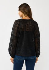 [Color: Black] A back facing image of a brunette model wearing a sheer crinkled chiffon blouse with all over embroidery. Featuring a split v-neckline with tie detail and a button front closure. 
